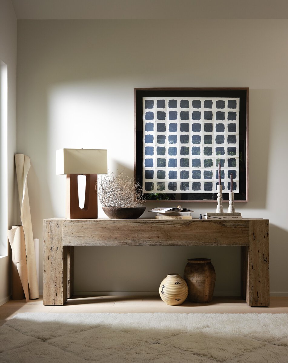 Wooden console table with decorative items against a neutral wall with a framed abstract painting.